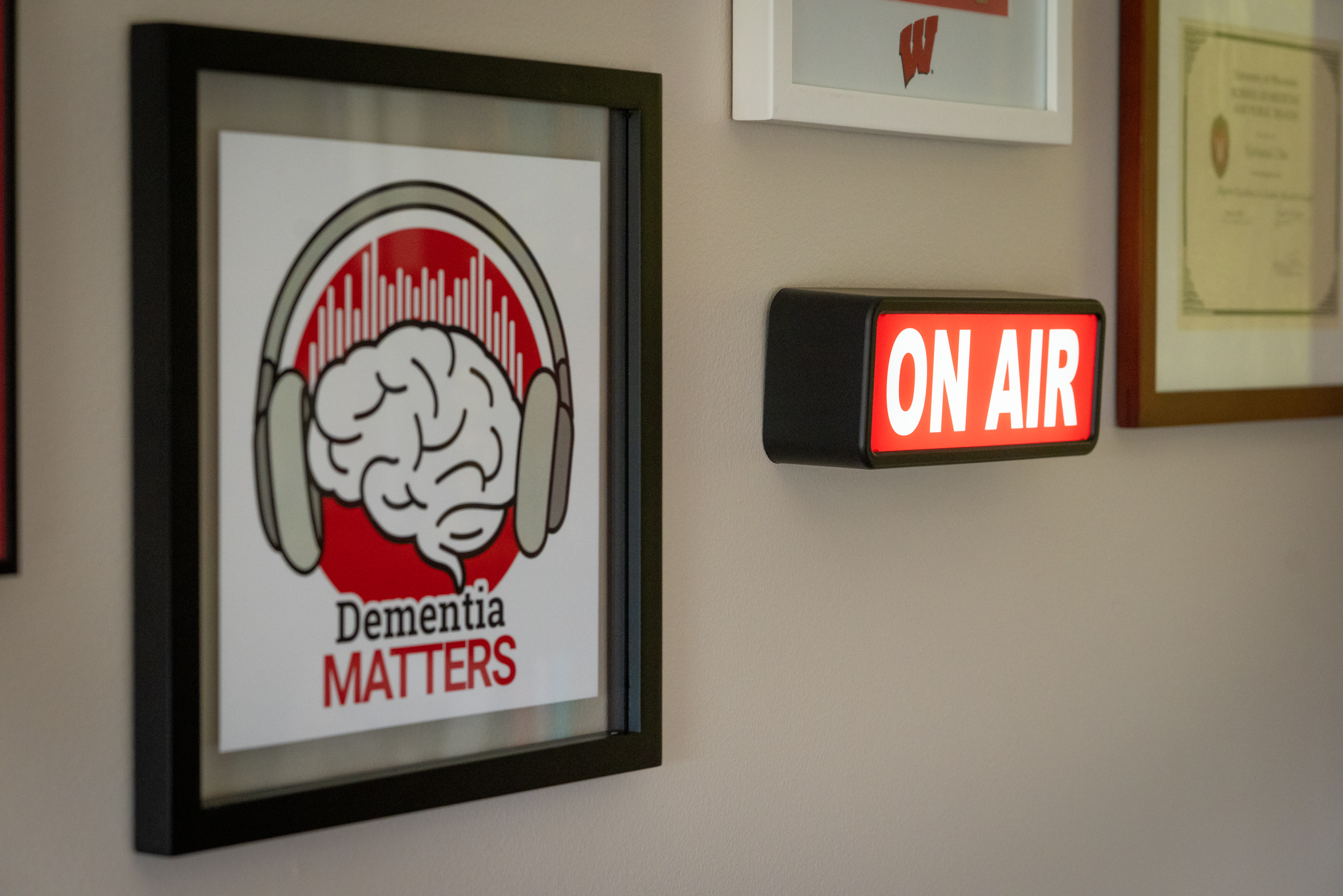 A framed picture of the Dementia Matters logo and a lit up "On Air" sign on a wall
