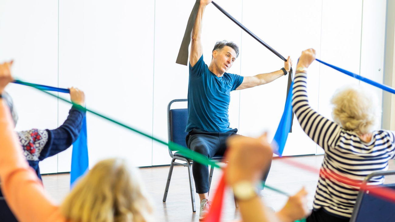 An instructor teaches a series of chair exercises to a class of older adults