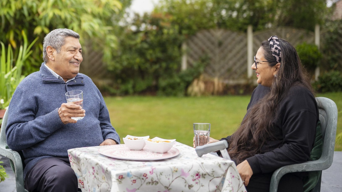 Two older adults enjoy some water and snacks out in their garden on a nice day