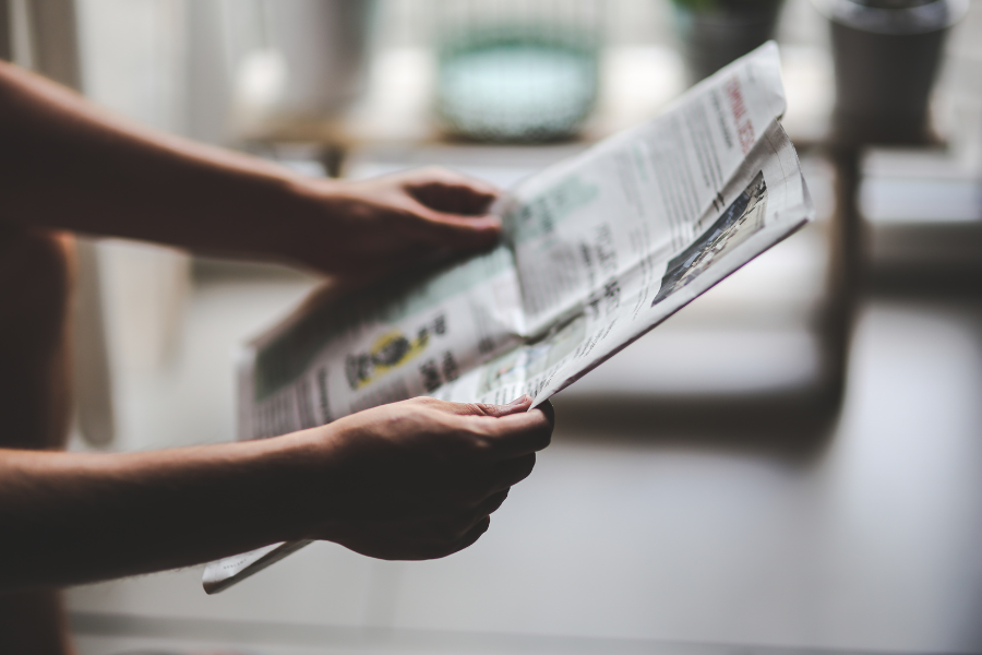 A person offscreen holds out a newspaper to read