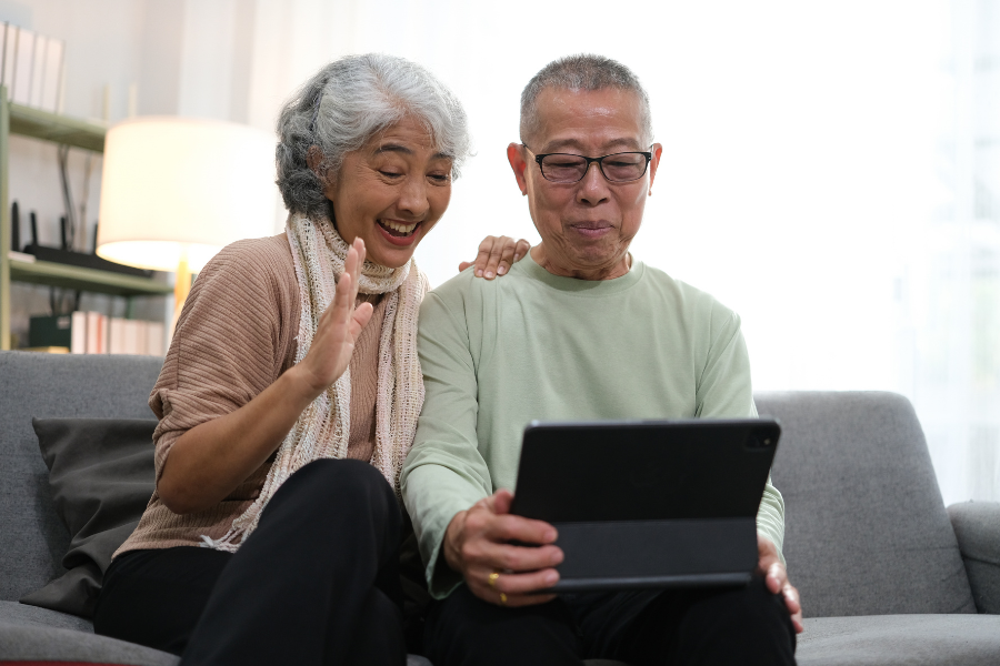 An older couple sit on the couch and watch something on a tablet in their laps