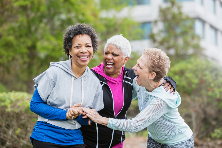 Three older woman stand together outside, laughing and smiling