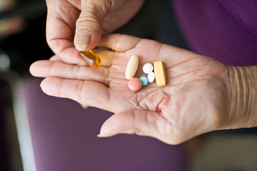 A person holds out their hand with a few different tablets and medications in it