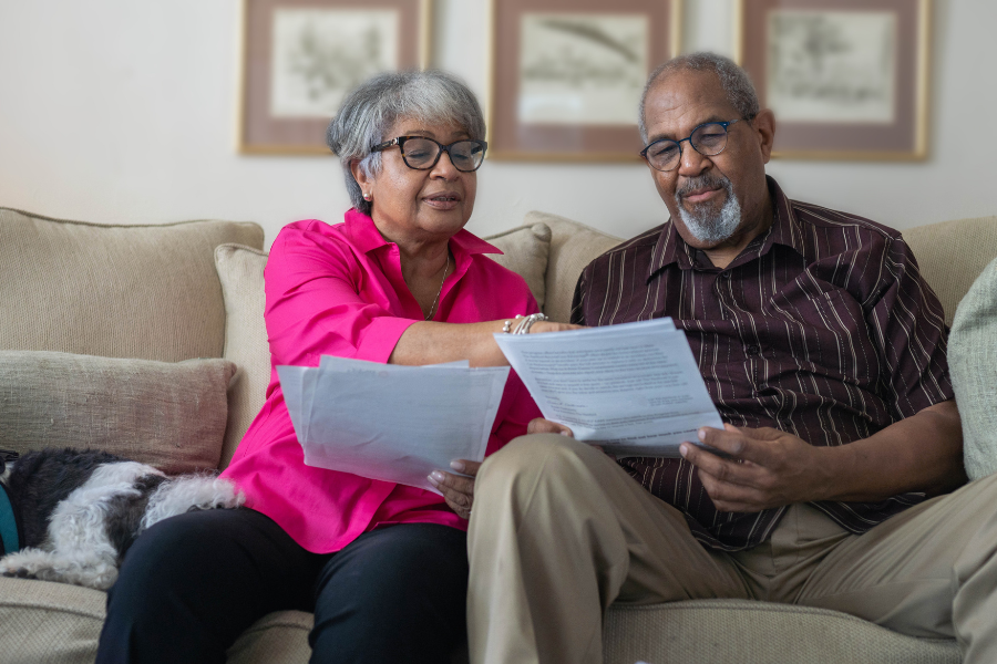 Two older adults sit on the couch and look through paperwork