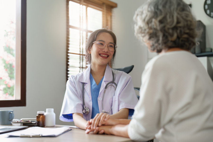 A doctor holds an older woman's hand while smiling while they talk